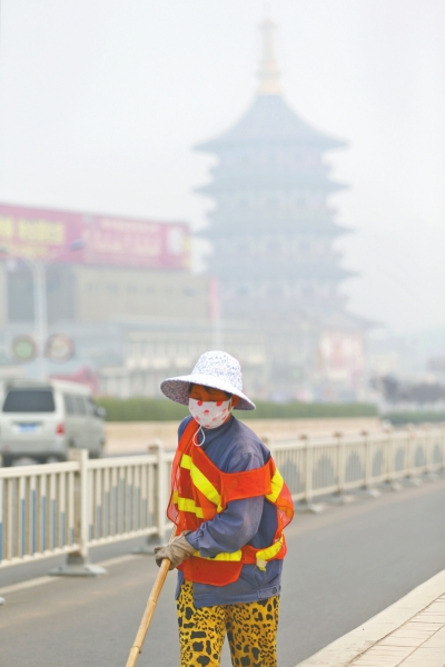 近日，在古都洛陽(yáng)，環(huán)衛(wèi)工人身后的“天堂”被霧霾籠罩著。