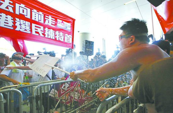 17日，在香港立法會外，一名反對政改的男子向支持派人群投擲標牌。