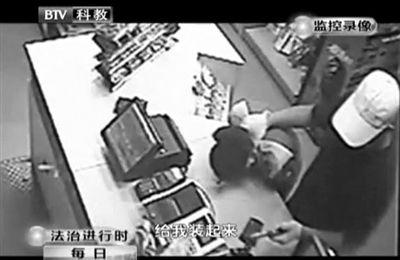 戴帽男子一手掐住加油站營(yíng)業(yè)員，一手持發(fā)令槍指向另一營(yíng)業(yè)員，要求“把錢(qián)給我裝起來(lái)”。