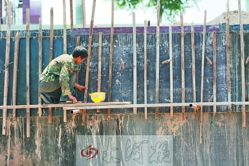 　　烈日下，狹窄的架子上，工人正用錘子固定樁基。