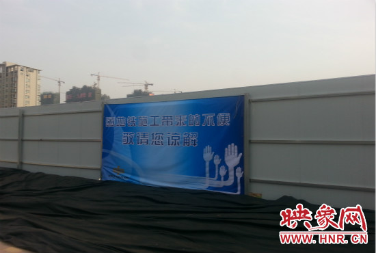 道路南側(cè)圍起了白色的圍擋，墻上標示著“因地鐵施工帶來的不便敬請您諒解”的提示牌。