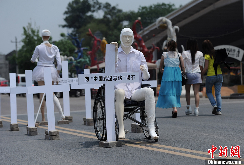 4月16日，重慶市洋人街上擺放著兩個受了傷的塑料人像“模特”，旁邊十字架上寫著向“中國式過馬路”說不