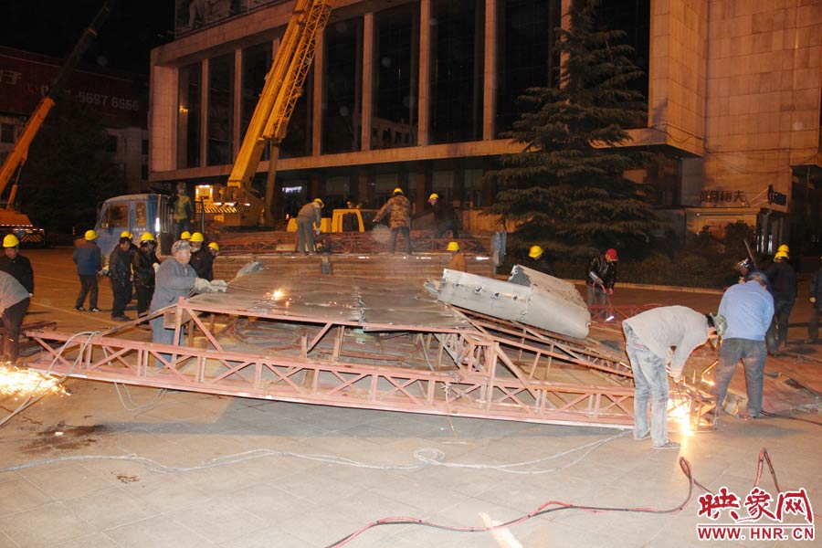 地面上的20多名工人對(duì)吊裝下的廣告牌進(jìn)行分割。