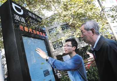 10月15日，滴滴工作人員（左）指導乘客使用“滴滴車站”的電子屏預約出租車。