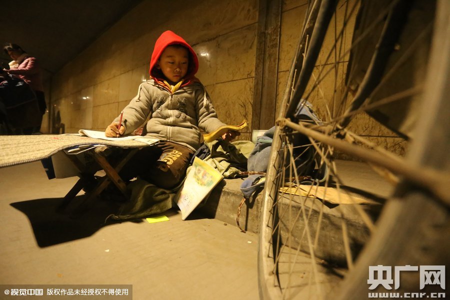 2015年11月8日晚，鄭州，7歲男孩涵洞橋下陪父母練攤，路邊燈下坐小馬扎上寫(xiě)作業(yè)。