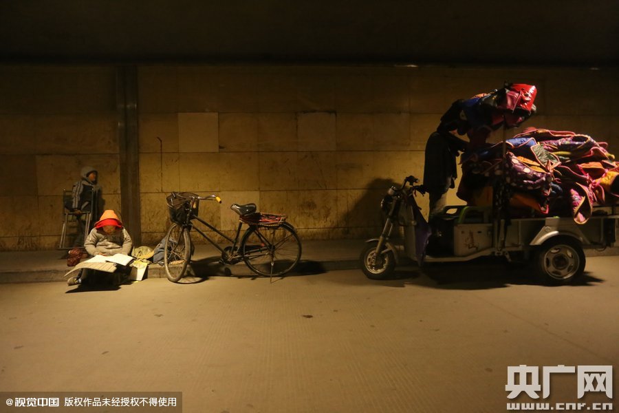 2015年11月8日晚，鄭州，7歲男孩涵洞橋下陪父母練攤，路邊燈下坐小馬扎上寫(xiě)作業(yè)。