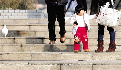 昨天中午，一女孩拉著家長(zhǎng)的手在紫荊山公園曬太陽(yáng)，氣溫升高，孩子的棉衣解開(kāi)了扣子。