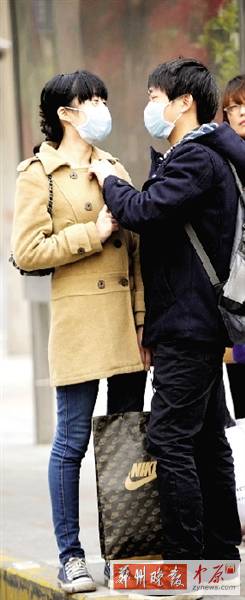 公交站臺(tái)上，一對年輕人戴著口罩，系緊衣領(lǐng)。